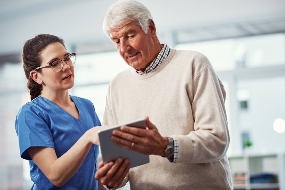 Nurse, tablet and healthcare with old man in home for routine structure, dementia schedule and retirement