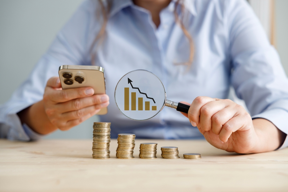 Businesswoman holding phone and magnifying glass examines income and expenses.