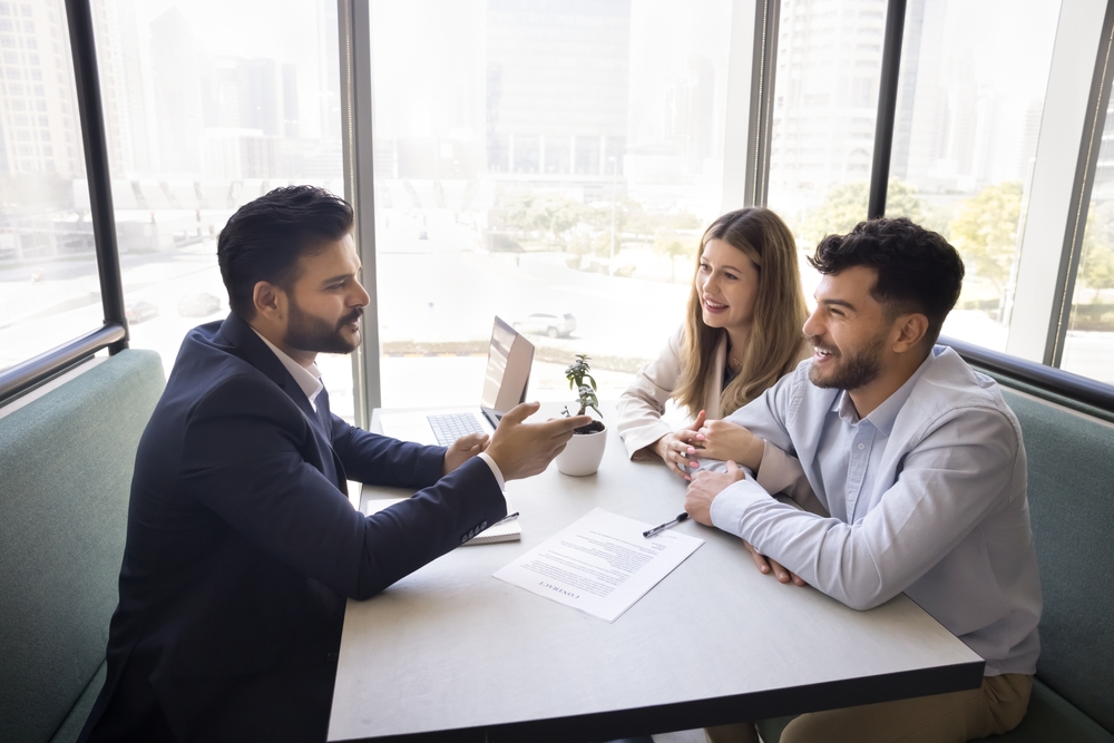 Positive male insurance agent real estate specialist win over multiethnic family couple of clients give professional advice in casual relaxed setting fostering trust comfort